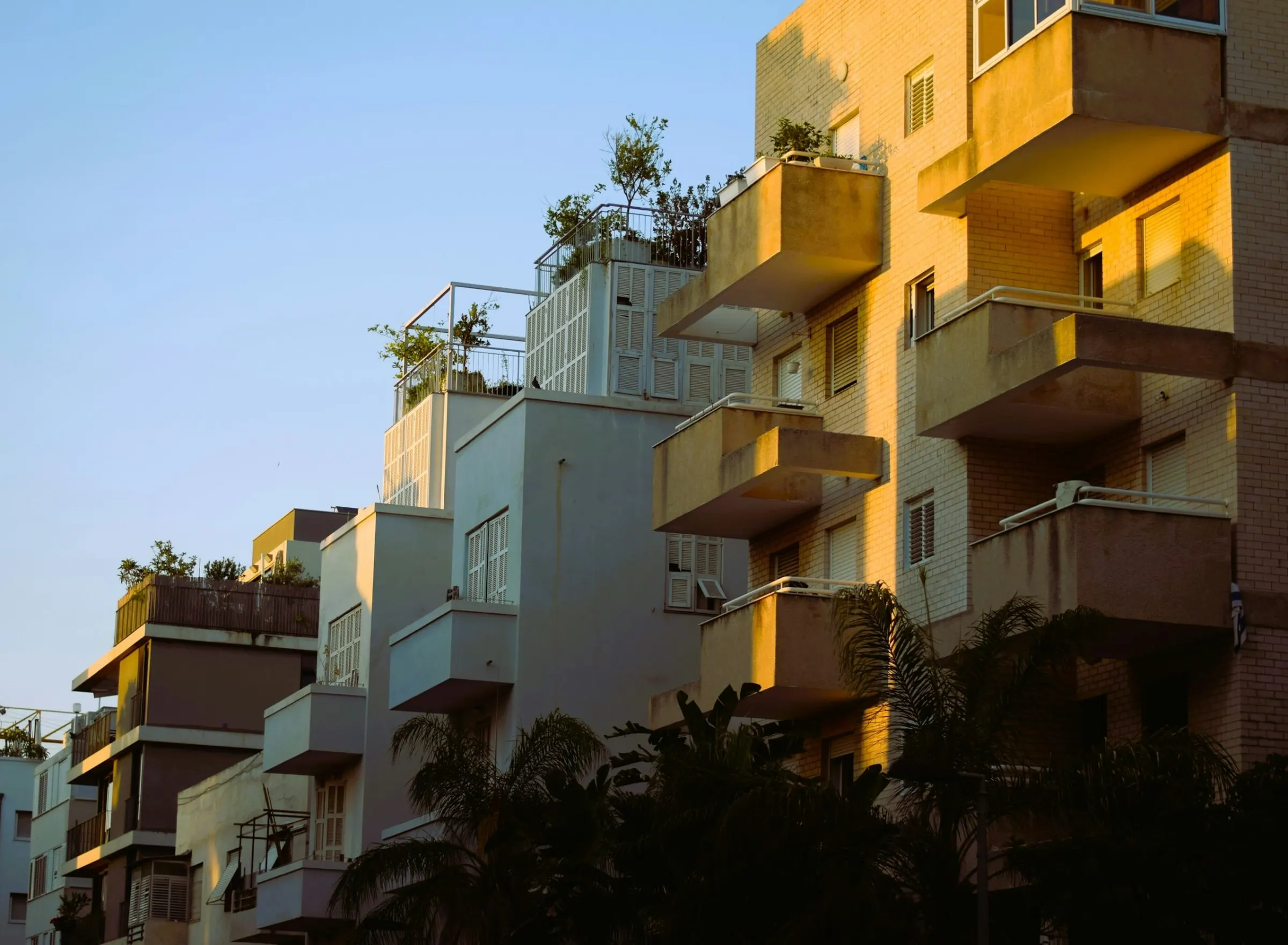 Edificio de apartamentos con balcones y palmas al atardecer